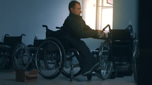 Side View of One American Male Workers in a Workshop at a Factory Making Wheelchairs Sitting at a