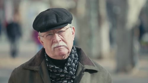 Wise Elderly Man in a Flat Cap and Glasses Standing in a Sunny Alley in Slo-mo