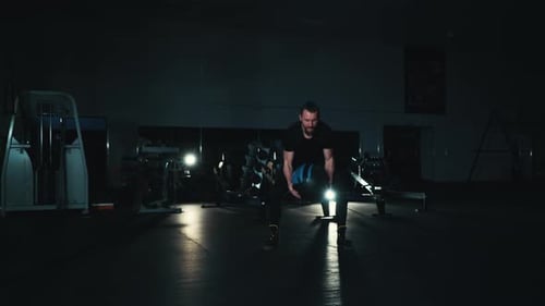 Fit Man Throwing Heavy Ball in Dark Gym