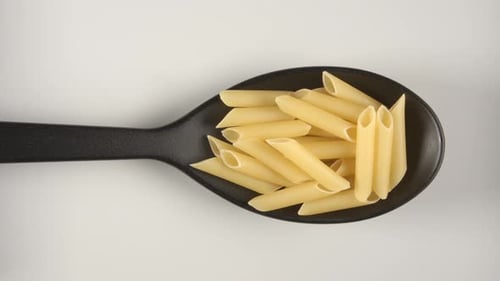 Penne Pasta Being Poured into Black Spoon