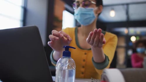 Caucasian woman wearing face mask using hand sanitizer at modern office