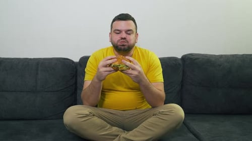 Man Eats Hamburger on a Couch