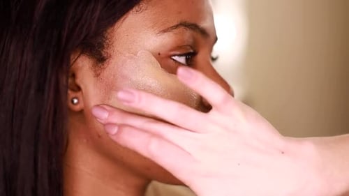 A female makeup artist applying gold makeup to a black African-American model.