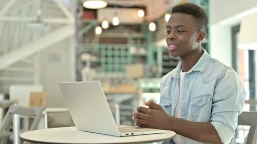 Young African Man Doing Video Chat on Laptop in Cafe