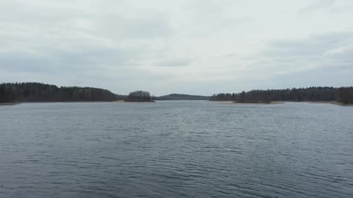 AERIAL: Rippling Water on the Surface of Lake with Forest in Background and Gloomy Sky in Horizon