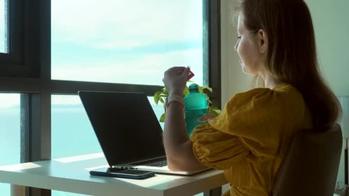 Junge Frau benutzt Laptop zu Hause und trinkt klares Süßwasser