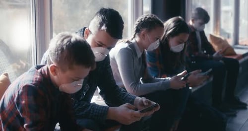 Teens in Masks Use Cellphones Indoors