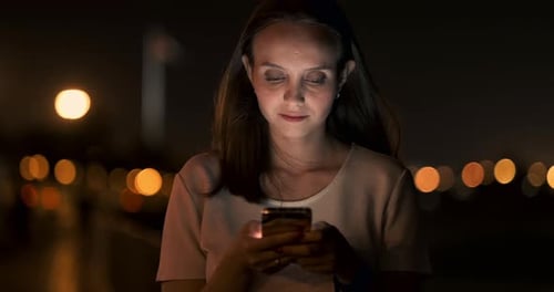 At Night a Young Girl Holds a Smartphone in Her Hands and Looks at the Screen