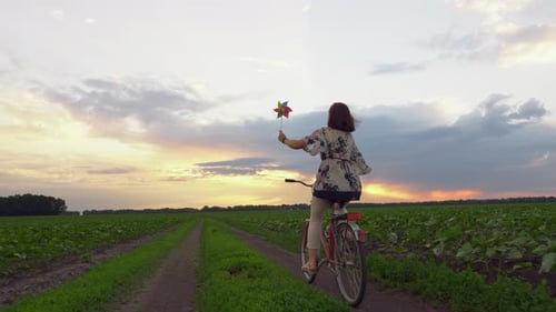Woman Rides Bicycle Through Fields at Sunset