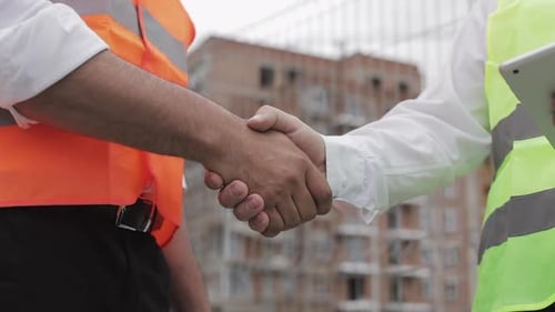 Zwei Architekten und Ingenieure beim Händeschütteln auf der Baustelle. Nahaufnahme.