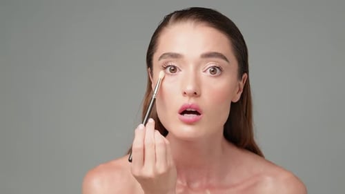 Woman Applies Eyeshadow with Makeup Brush in Studio