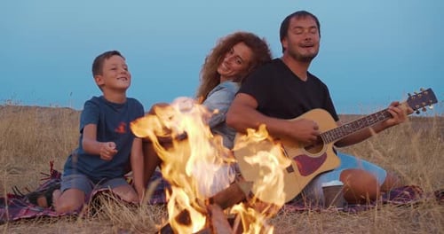 Daddy Plays Guitar , Mom with Son Enjoy While Relaxing on Family Picnic Near Bonfire. Close-up.