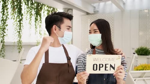 Business owner attractive young Asian in apron hanging we're open sign