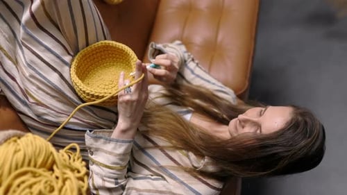 Woman Crocheting Yellow Basket on Couch at Home