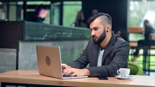 Jeune indépendant concentré avec une coiffure tendance travaillant sur un ordinateur portable assis au café public