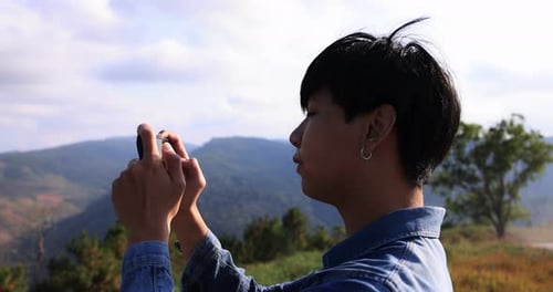 Young Asian traveler taking video with smart phone on top of the mountain.