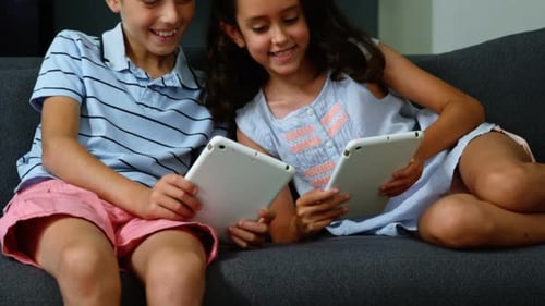 Boy and Girl Play on Tablets on Couch