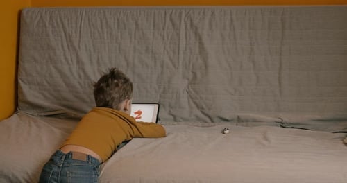 Boy Using Tablet Computer Lying on Bed
