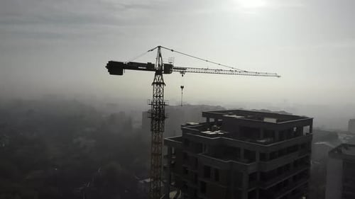 Birds eye view on tower crane in fog standing next to residential building.