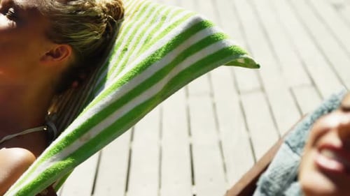 Two womens lying on deck chairs sunbathing near swimming pool