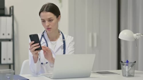 Doctor Using Smart Phone and Laptop in Office
