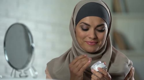 Woman Applies Moisturizer in Front of Mirror