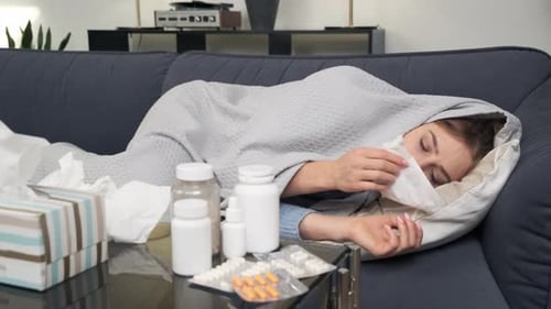 Une jeune femme malade avec de la fièvre s'essuie le nez avec une serviette recouverte d'une couverture ayant des symptômes de grippe