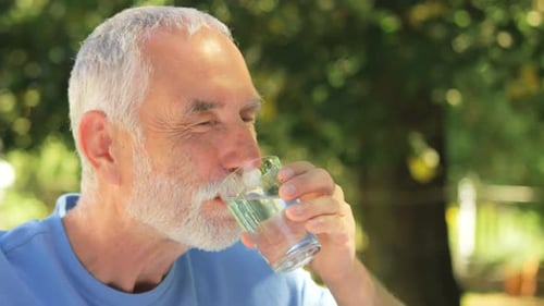 Senior man drinking water in glass at garden