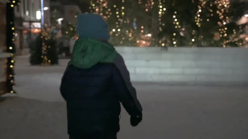 Child running in snowy street with Christmas lights