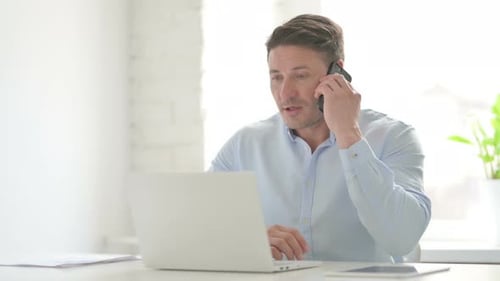 Man Talking on Phone while using Laptop in Office