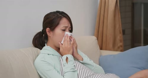 Young Woman Wipes Nose with Tissue Indoors