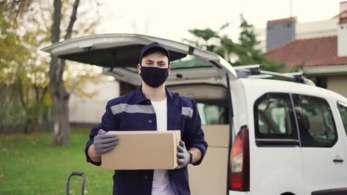 Schöner Kurier holt Kartonpaket aus dem Lieferwagen und geht durch den privaten Sektor