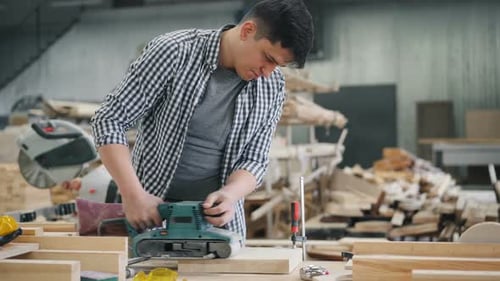 Young Man Working in Wood Workshop Using Polishing Machine To Polish Wood