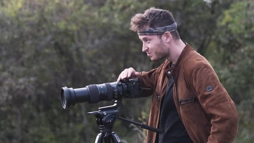 Man Setting Up Camera on Tripod Outdoors
