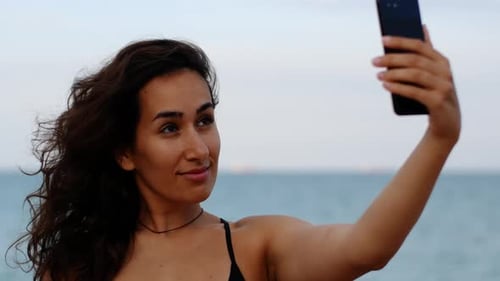 Beautiful sexy tanned woman makes selfie in the background of the sea. Woman makes summer photo