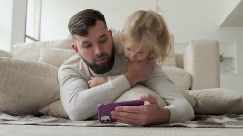 Bearded Man and Child Watching Phone on Sofa