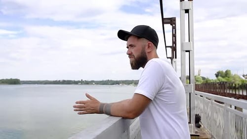 Man Looking at Peaceful Waterscape on Bridge