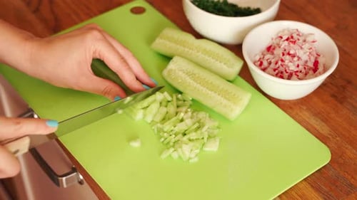 Woman Is Slicing Fresh Cucumber in the Kitchen on Wooden Table