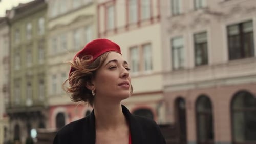 Portrait Of Stylish Young Woman In Red Beret. Woman Looking At Houses On City Square.