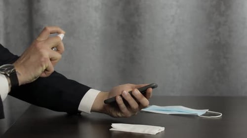 Adult Disinfecting Smartphone at Table with Mask
