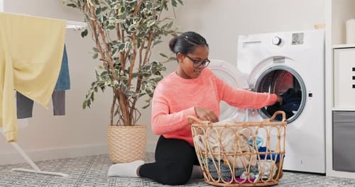 Woman in Glasses Performs Household Chores in Bathroom Laundry Room Kneels with Wicker Basket Filled