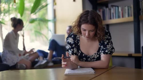 Ein junges nachdenkliches Mädchen sitzt in der Bibliothek und schreibt in ein Notizbuch