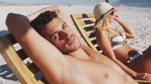 Caucasian couple sitting on sunbeds on the beach