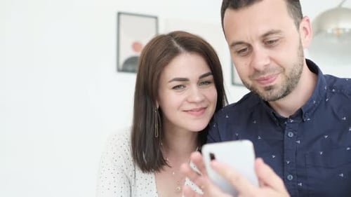 Smiling Couple Looking at Smartphone in Bright Home