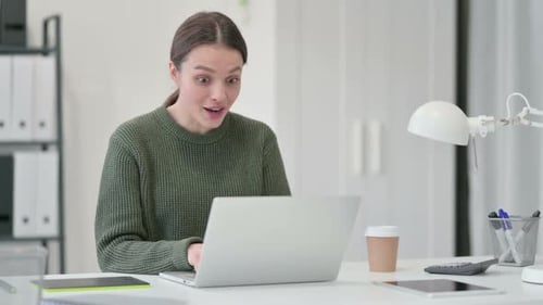 Young Woman Celebrating Success at Workplace Desk