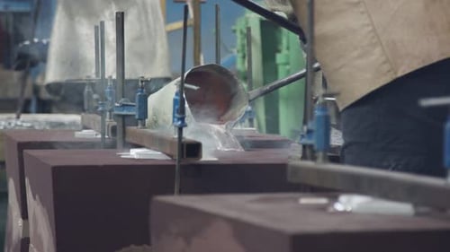 Workers in a foundry pouring liquid Aluminum to a sand cast