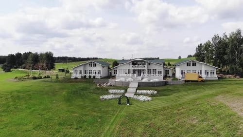 Aerial View of a Country Cottage with a Terrace with Tables and a Lawn with a Flower Arch and Rows