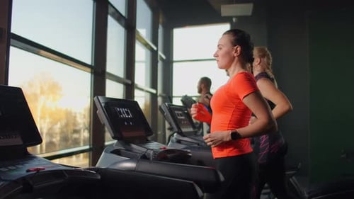 Cute Young Girl Running on a Treadmill in Front of Panoramic Windows in the Fitness Room. Gym with