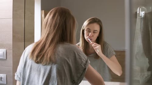 Woman Brushing Teeth in Bathroom Mirror