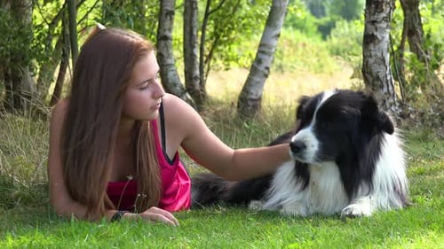 Eine Frau und ein Border Collie liegen auf Gras auf einer Wiese, die Frau streichelt gelegentlich den Hund und schaut